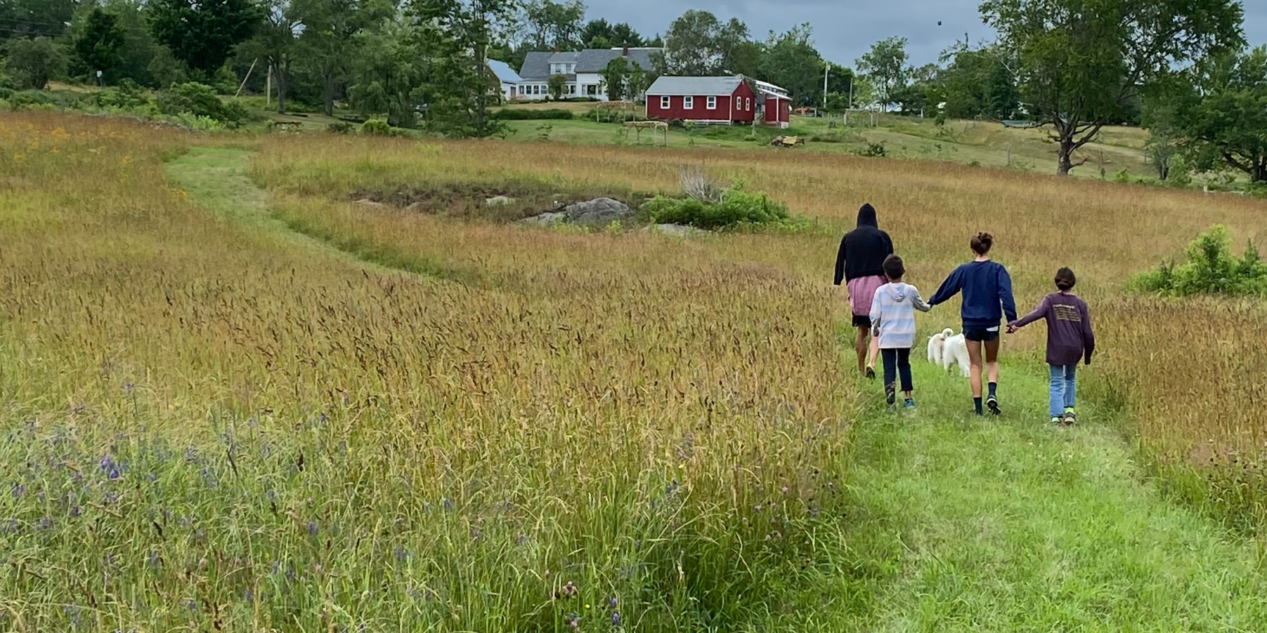 Kids hiking through the farm fields at Pumpkin Vine Family Farm with the farm and red barn in the background.
