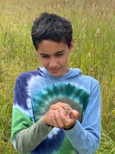 Teen in tye dye releasing a rescued and rehabbed bob link into Pumpkin Vine Family Farm fields.