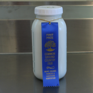 A glass jar of pumpkin vine family farm goats milk with a blue ribbon around it as an award from the Common Ground Country Fair in Unity, ME