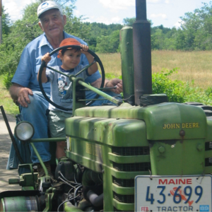 Little boy and older man on an old green john deer tractor with a Maine license plate