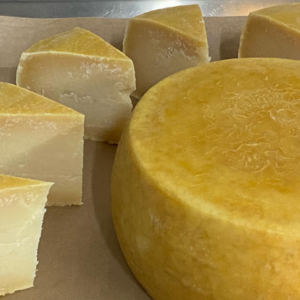 A full wheel and slices of Pumpkin Vine Family Farm's capriccio cheese on brown paper.