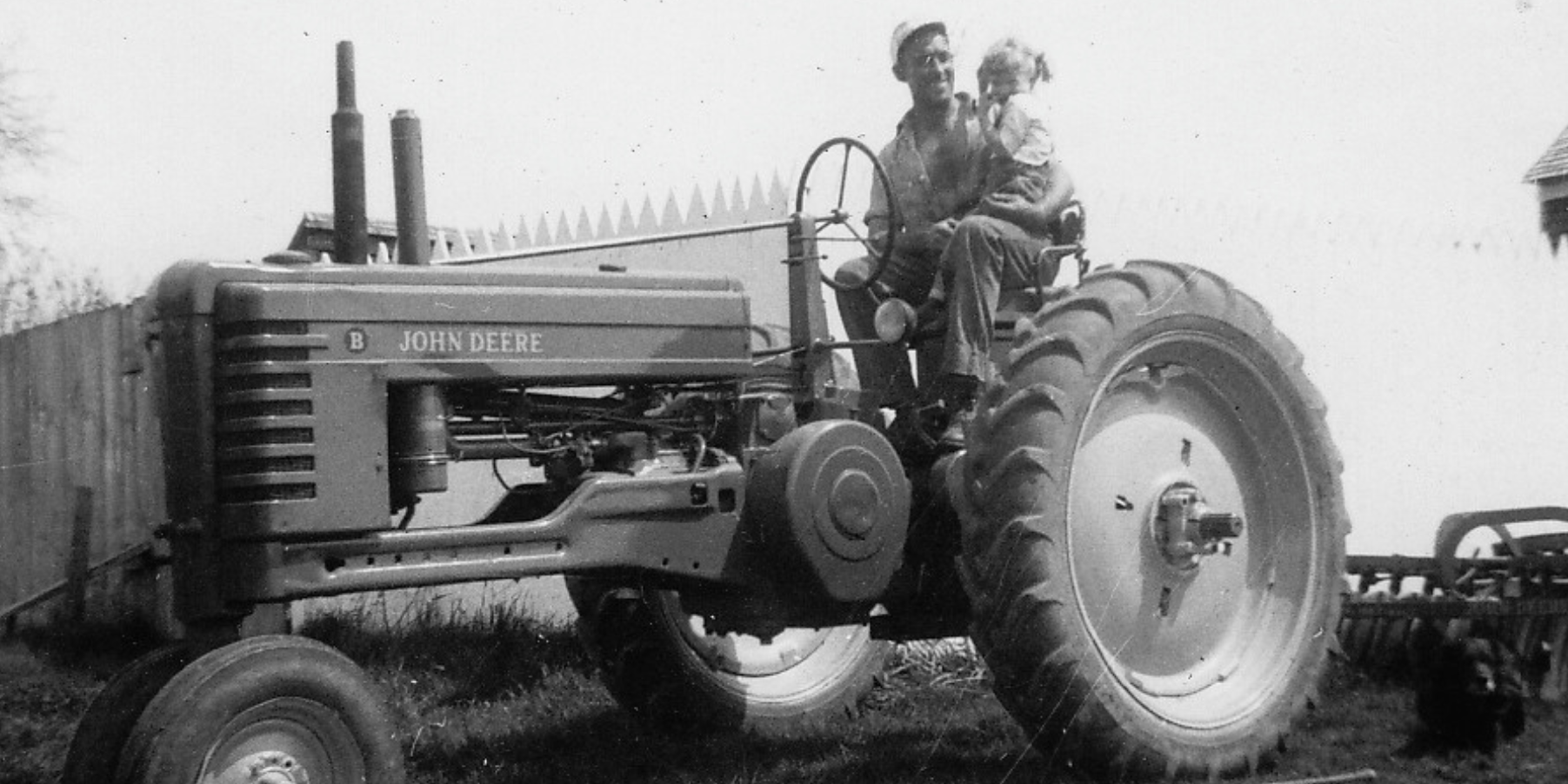 Old black and white image of a man and child on an old john deere tractor in Somerville, Maine.