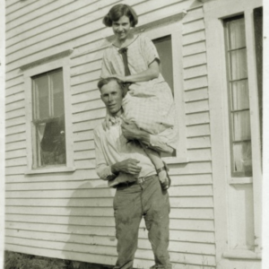 black and white of new husband holding new wife on his shoulder in front of their family farm house.