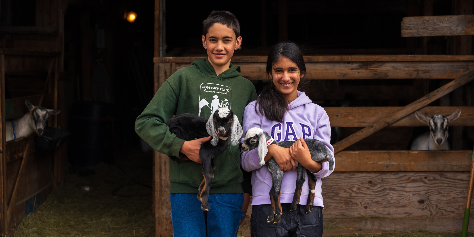Young boy and girl with two baby goats at the enterance to the barn at Pumpkin Vine farm in Midcoast Maine.