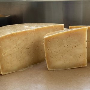 pvff teleporter cheese wedges (slight brownish cheese with pock marks on sides) sitting on a table made at Pumpkin Vine Family Farm in Somerville, ME.