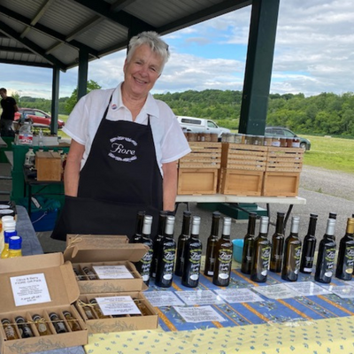 Judy from FIORE olive oils at a Farmers Market table with the olive oils and vinegars she is selling.