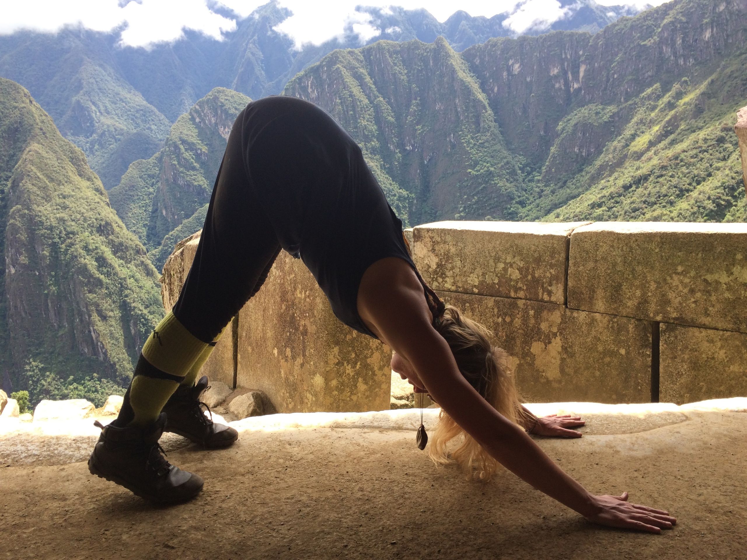 A woman in downward dog yoga pose with huge mountains in the background.