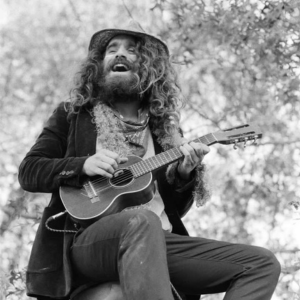black and white image of musician heavy meadow sitting outside playing a small guitar.