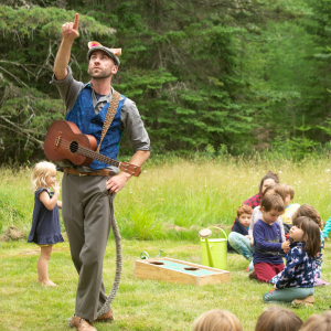 Performing the Petra and Mo Show in a green field with a small guitar.