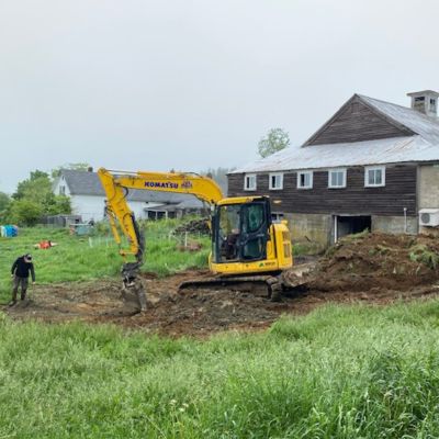 big yellow excavator in a green field digging the new foundation for the milking parlor.